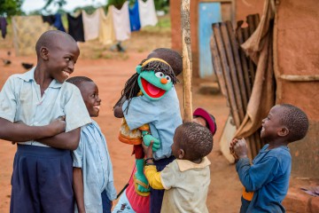Having Fun with a Muppet, by Dr Greg Allgood, WVUS
Children from the Chalimbana Primary School WASH club, in Chongwe ADP, Zambia, meet one of the newest Sesame Street Muppets called Raya. She’s a 6 year-old green girl that knows a lot about clean water, sanitation, and hygiene.  What a coincidence that she was born on World Water Day! Raya is getting some help from her friend Elmo.
Sesame Street is the largest informal educator of children in the world and has characters that help address important social causes including HIV and obesity. 
World Vision believes that children can be powerful agents of positive change in communities and because of this, a critical part of World Vision water, sanitation, and hygiene (WASH) programs in the developing world includes outreach to schools. World Vision reaches an amazing 4 new schools every day with clean water, sanitation, and hygiene. World Vision has learned that children can not only receive important messages about healthy habits but they can also deliver these messages effectively to their brothers, sisters, and parents.   By doing this, they can dramatically change the health of a community.  And, importantly, kids respond best when they’re having fun while they learn.
Sesame Street and World Vision have partnered to leverage each other’s strengths to help end the global water, sanitation, and hygiene crisis.
The educational activities are focused on after school WASH clubs.   The curriculum has been developed using the expertise of both Sesame Street and World Vision.  By working with Zambian educational experts the curriculum can be adapted to the local context. 
The result is a “WASH-Up kit” that can be provided to a school. It includes two floor mats that include games to teach the proper behaviors.   One mat uses a slide and ladder game, the other is like Twister, with places to step. Flip charts featuring Sesame characters are used to teach the children. It’s simple to use and an engaging teac